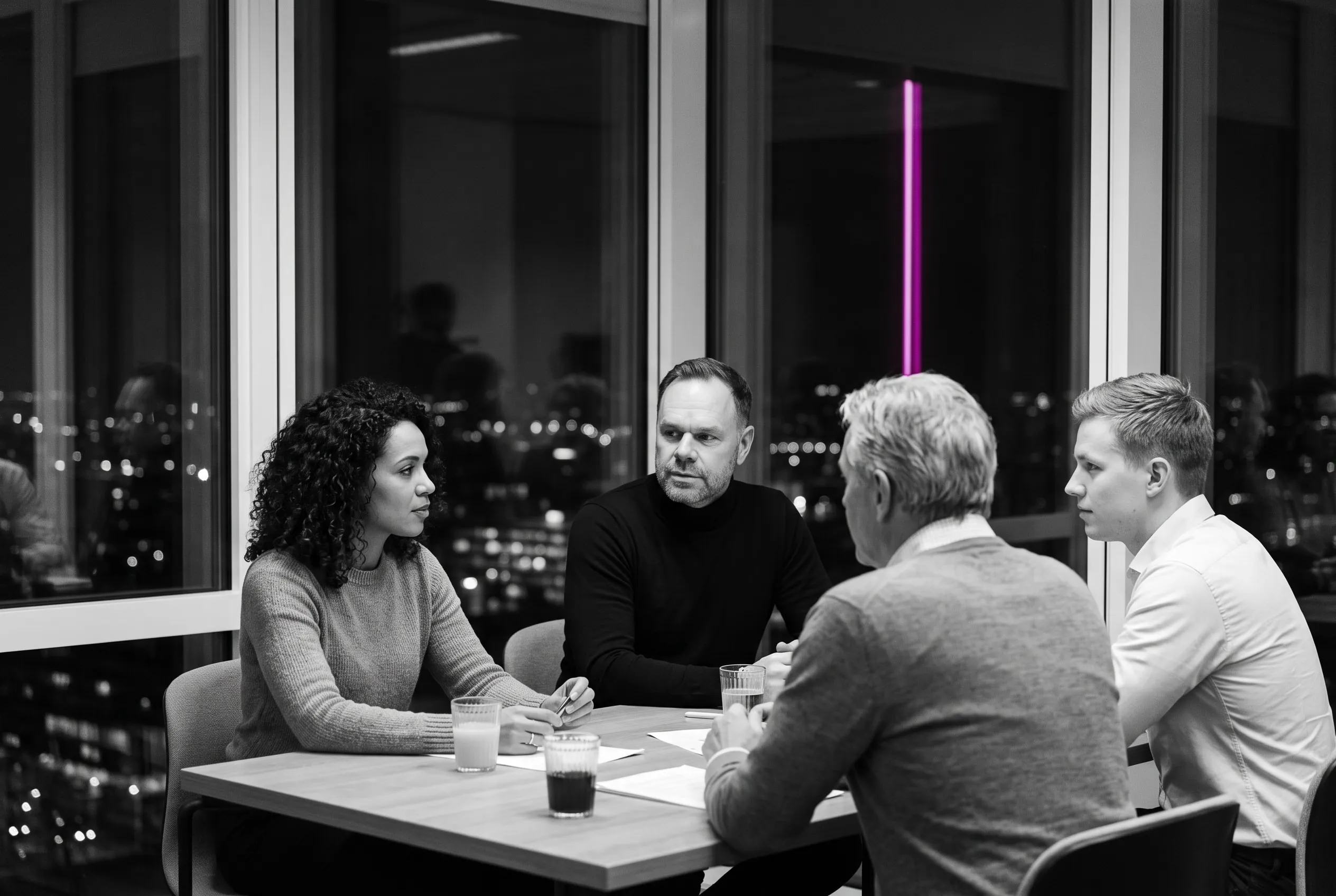 Helge Weiss in a black turtleneck at a meeting table with colleagues, city lights beyond the window at night.
